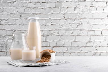 Vegan günlük olmayan karabuğday sütü şişede, sürahide ve bardakta karabuğday homurdanmaları kasede ve beyaz taş masada. Vegan karabuğday içeceği, bitki bazlı alternatif süttür. Sebzeler sağlıklı süt ürünü