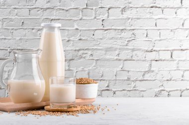 Vegan günlük olmayan karabuğday sütü şişede, sürahide ve bardakta karabuğday homurdanmaları kasede ve beyaz taş masada. Vegan karabuğday içeceği, bitki bazlı alternatif süttür. Sebzeler sağlıklı süt ürünü