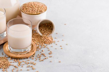 Vegan günlük olmayan karabuğday sütü bardakta ve beyaz taş masadaki bir kasede karabuğday homurdanması. Vegan karabuğday içeceği, bitki bazlı alternatif süttür. Sebzeler sağlıklı süt ürünü, kopyalama alanı