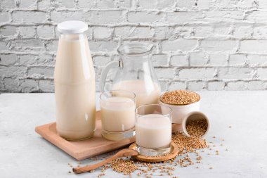 Vegan günlük olmayan karabuğday sütü şişede, sürahide ve karabuğday dilimli bardaklarda beyaz taş masadaki kasede. Vegan karabuğday içeceği, bitki bazlı alternatif süttür. Sebzeler sağlıklı süt ürünü
