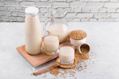 Vegan günlük olmayan karabuğday sütü şişede, sürahide ve karabuğday dilimli bardaklarda beyaz taş masadaki kasede. Vegan karabuğday içeceği, bitki bazlı alternatif süttür. Sebzeler sağlıklı süt ürünü