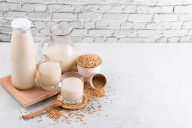 Vegan günlük olmayan karabuğday sütü şişede, sürahide ve karabuğday homurdanması dolu bardaklarda beyaz taş bir masada.