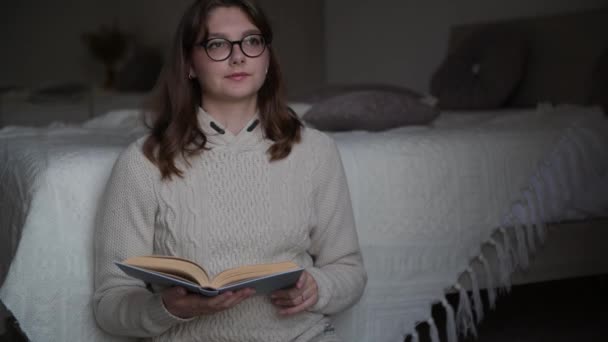 眼鏡で4Kの若い女性は セーターを着て パンパス草と居心地の良い巨大な部屋で本を読んでいる ページをめくる リラクゼーション 家で居心地の良い冬の日 — ストック動画