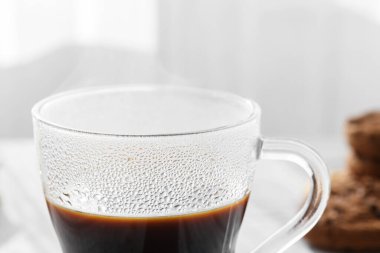 Sabah gölgeli şeffaf bir fincan sıcak kahve ve gri masa arkaplanındaki pencereden güneş ışınları, yakın çekim. Sabah kahve konsepti