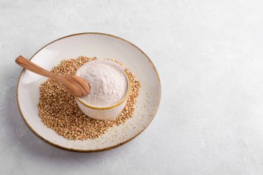 Kaşık ve çiğ yeşil karabuğday tanesiyle seramik tabakta açık gri beton arka planda karabuğday unu, üst manzara. Alternatif un, glütensiz un, sağlıklı beslenme.