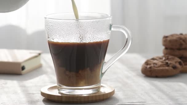 牛奶在透明的咖啡杯里倒入新鲜咖啡 旁边是巧克力曲奇饼 有晨影和晨光 背景是灰色的桌子 — 图库视频影像