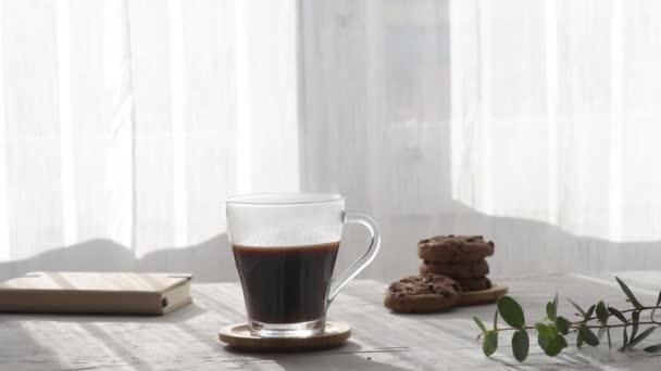 灰色のテーブルの背景の窓を通して朝の影と太陽の光線で熱いコーヒーカップを蒸す スチームズーム付きのホット透明ガラスコーヒーカップ ホットコーヒードリンクのコンセプト — ストック動画