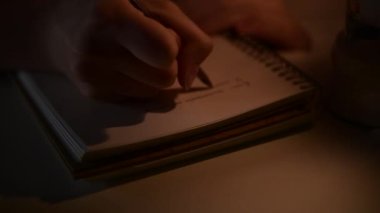 4k Hand writes poeme in notebook with flickering candle light, writing poetry, inspiration concept, creativity and art at night, close up