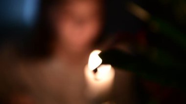 4k The girl looks at a burning candle, close-up. Out of focus camera, focuses on the girl and the flame