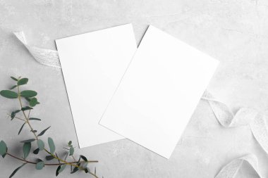Tarafsız gri mermer arka planda okaliptüs yapraklı iki düğün davetiyesi.