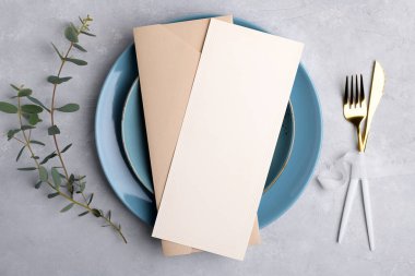 Menu card mockup with envelope on blue plate with festive table setting with eucalyptus branch on grey background clipart