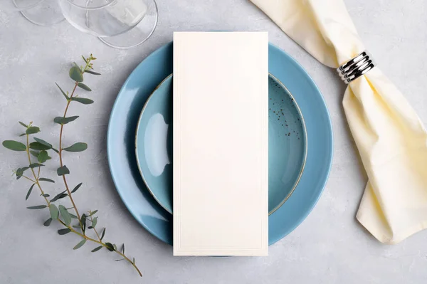 Menu card mockup on blue plate with festive wedding or birthday table setting with eucalyptus branch on grey background — стоковое фото