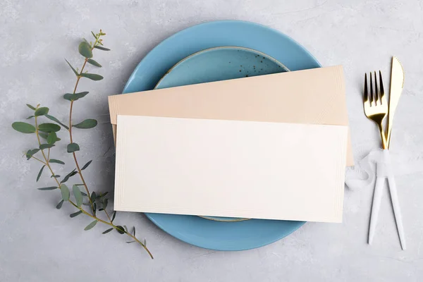 Invitation card mockup with envelope on blue plate with festive table setting with eucalyptus branch on grey background — стоковое фото