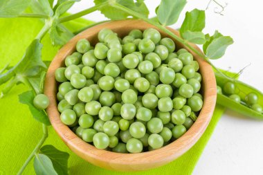 Tahta bir kasede taze yeşil bezelyeler ve bezelye bitkileri beyaz arka planda yeşil bir peçete üzerinde yeşil yapraklar, sağlıklı fasulye proteinleri.