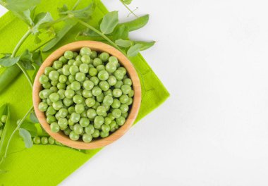 Tahta bir kasedeki taze bezelyeler bezelye bitkileriyle beyaz arka plandaki peçeteye yapraklar sağlıklı fasulye proteinleri, üst görüş.