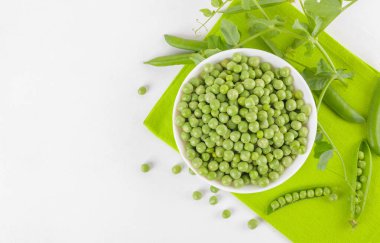 Bezelye bitkileriyle bezelye kabındaki taze bezelyeler beyaz arka plandaki peçeteye yapraklar sağlıklı fasulye proteinleri, üst görünüm.