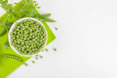 Bezelye bitkileriyle bezelye kabındaki taze bezelyeler beyaz arka plandaki peçeteye yapraklar sağlıklı fasulye proteinleri, üst görünüm.