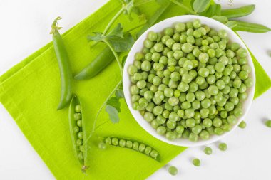 Bezelye bitkileriyle bezelye kabındaki taze bezelyeler beyaz arka plandaki peçeteye yapraklar sağlıklı fasulye proteinleri, üst görünüm.
