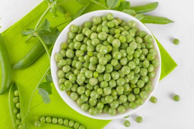 Bezelye bitkileriyle bezelye kabındaki taze bezelyeler beyaz arka plandaki peçeteye yapraklar sağlıklı fasulye proteinleri, üst görünüm.