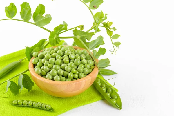 Fresh green peas in a wooden bowl with peas plants leaves on a green napkin on white background, Healthy bean protein — ストック写真