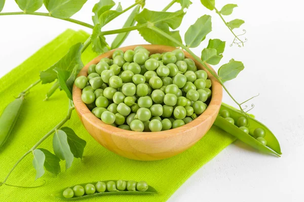 Fresh green peas in a wooden bowl with peas plants leaves on a green napkin on white background, Healthy bean protein — ストック写真