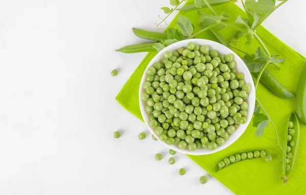 Bezelye bitkileriyle bezelye kabındaki taze bezelyeler beyaz arka plandaki peçeteye yapraklar sağlıklı fasulye proteinleri, üst görünüm.