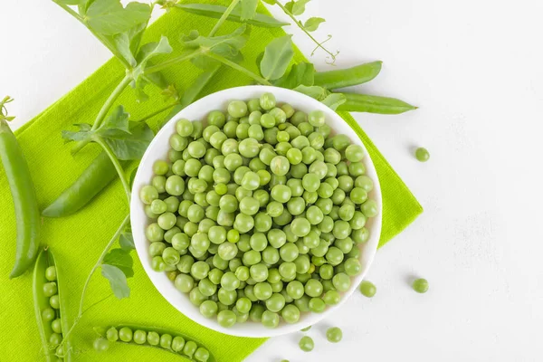 Bezelye bitkileriyle bezelye kabındaki taze bezelyeler beyaz arka plandaki peçeteye yapraklar sağlıklı fasulye proteinleri, üst görünüm.