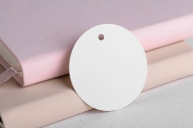 Round white gift tag mockup on beige and pink book background. Blank paper circular price sticker tag mockup, Sale and Black Friday concept, element for design, label mockup