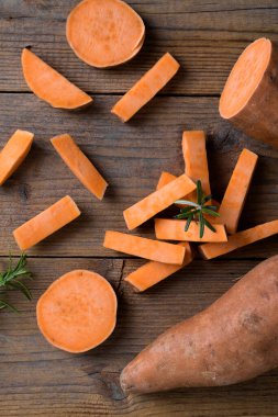 Çiğ portakallı tatlı patates ve taze biberiyeli yarasa dilimleri ahşap arka planda, üst görünümde, dikey yönelimde.