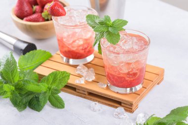 Soğuk yaz çilekli mojito, margarita, daiquiri. İki bardak taze çilekli soda, buz küpleri ve açık gri arka planda nane yaprakları. Buzlu çilekli limonata, yakın çekim.
