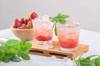 Soğuk yaz çilekli mojito, margarita, daiquiri. İki bardak taze çilekli soda, buz küpleri ve beyaz arka planda nane yaprakları. Buzlu çilekli limonata, yakın çekim.