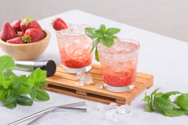 Soğuk yaz çilekli mojito, margarita, daiquiri. İki bardak taze çilekli soda, buz küpleri ve açık gri arka planda nane yaprakları. Buzlu çilekli limonata, yakın çekim.