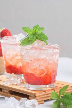 Soğuk yaz çilekli mojito, margarita, daiquiri. İki bardak taze çilekli soda, buz küpleri ve açık gri arka planda nane yaprakları. Buzlu çilekli limonata, yakın çekim.