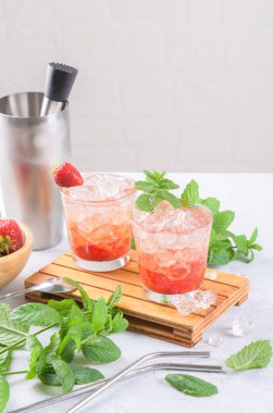 Soğuk yaz çilekli mojito, margarita, daiquiri. İki bardak taze çilekli soda, buz küpleri, nane şekeri ve açık arkaplanda barmen aletleri. Buzlu çilekli limonata, yakın çekim.