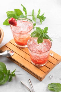 Soğuk yaz çilekli mojito, margarita, daiquiri. İki bardak taze çilekli soda, buz küpleri ve açık gri arka planda nane yaprakları. Buzlu çilekli limonata, yakın çekim.