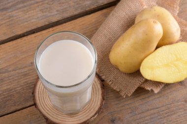Bardakta vegan patates sütü ve kırsal ahşap arka planda patates yumrusu. Kapatın. Bitki bazlı alternatif süt değiştirici ve laktozsuz, sağlıklı vejetaryen ve vejetaryen içecek konsepti