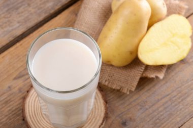 Bardakta vegan patates sütü ve kırsal ahşap arka planda patates yumrusu. Kapatın. Bitki bazlı alternatif süt değiştirici ve laktozsuz, sağlıklı vejetaryen ve vejetaryen içecek konsepti