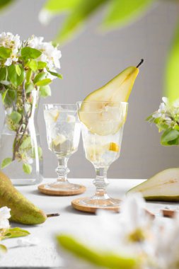 Armut kokteyli, armut püresi, taze meyve ve açık gri arka planda çiçekler. Yaz aylarında soğuk armut, masada buzlu limonata, çiçekli dallı köpüklü Mocktail tatlı içeceği.