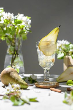 Armut kokteyli, armut püresi, taze meyve ve açık gri arka planda çiçekler. Yaz aylarında soğuk armut, masada buzlu limonata, çiçekli dallı köpüklü Mocktail tatlı içeceği.