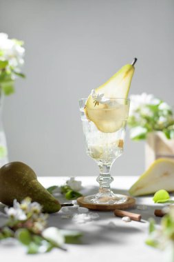 Armut kokteyli, armut püresi, taze meyve ve açık gri arka planda çiçekler. Yaz aylarında soğuk armut, masada buzlu limonata, çiçekli dallı köpüklü Mocktail tatlı içeceği.