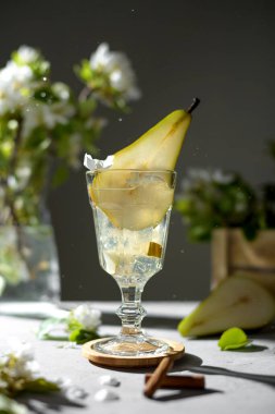 Armut kokteyli, armut püresi, taze meyve ve gri arka planda çiçekler ve gölgeler. Yaz aylarında soğuk armut, masada buzlu limonata, çiçekli dallı köpüklü moktail tatlı içeceği
