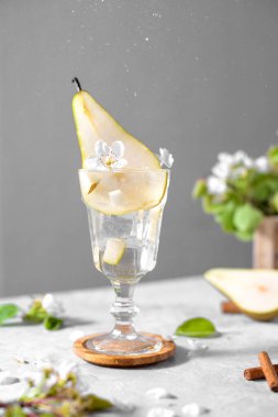Açık gri arka planda taze meyve ve çiçeklerle süslenmiş bir bardakta armut kokteyli. Yaz aylarında soğuk armut, masada buzlu limonata, çiçekli dallı köpüklü moktail tatlı içeceği