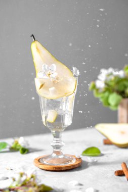 Açık gri arka planda taze meyve ve çiçeklerle süslenmiş bir bardakta armut kokteyli. Yaz aylarında soğuk armut, masada buzlu limonata, çiçekli dallı köpüklü moktail tatlı içeceği