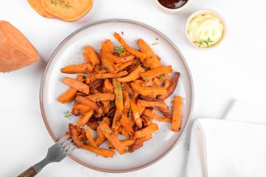 Seramik tabakta tavada kızartılmış sebzeli, tuzlu ve biberli nefis ev yapımı tatlı patates, ketçap ve barbekü sosu açık gri masa arka planında.