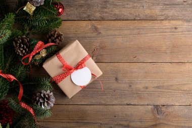Christmas fir tree decoration frame with gift on rustic wooden background. Christmas background with fir branches, red berries, cones, flat lay and copy space, element for design