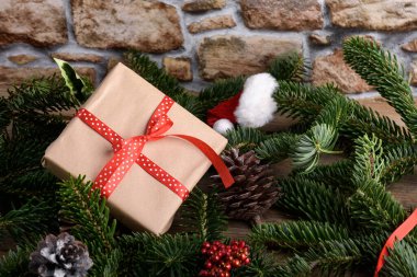 Kırsal ahşap arka planda kırmızı kurdeleli Noel Kraft hediye kutusu, Noel arkaplanı, doğal köknar dalları, koniler, rahat Noel natürmortu, yeni yıl yatağı, üst manzara