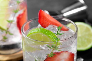 Cold summer strawberry cocktail mojito, margarita, daiquiri. Two glasses with fresh strawberry soda drink, ice cubes, thyme and bartender tools on dark background. Iced strawberry lemonade, close up