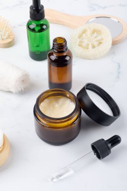 Opened moisturizer cream jar and essential or lotion in amber glass bottle and set of skin and bodycare products on white background. Cosmetic packaging mockup. Natural cosmetics home skincare routine