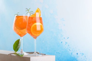 Classic italian aperitif aperol spritz cocktail in two wineglasses with ice cubes and slice of orange with light blue background on marble stone podium, traditional summer fresh iced drink, close up