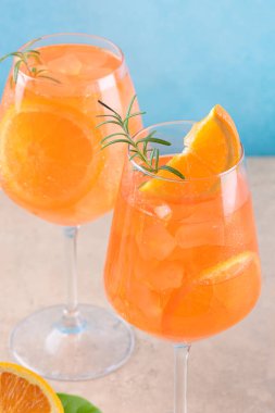 Classic italian aperitif aperol spritz cocktail in two wineglasses with ice cubes and slice of orange with light blue background on beige stone background, traditional summer fresh iced drink, closeup